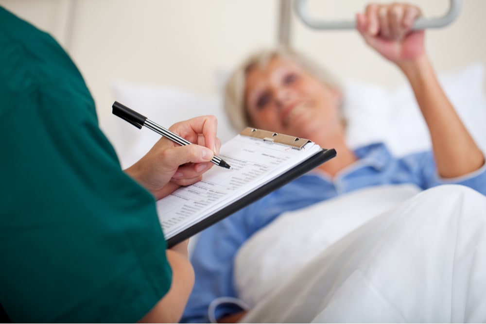 female nurse writing on clipboard while looking at patient